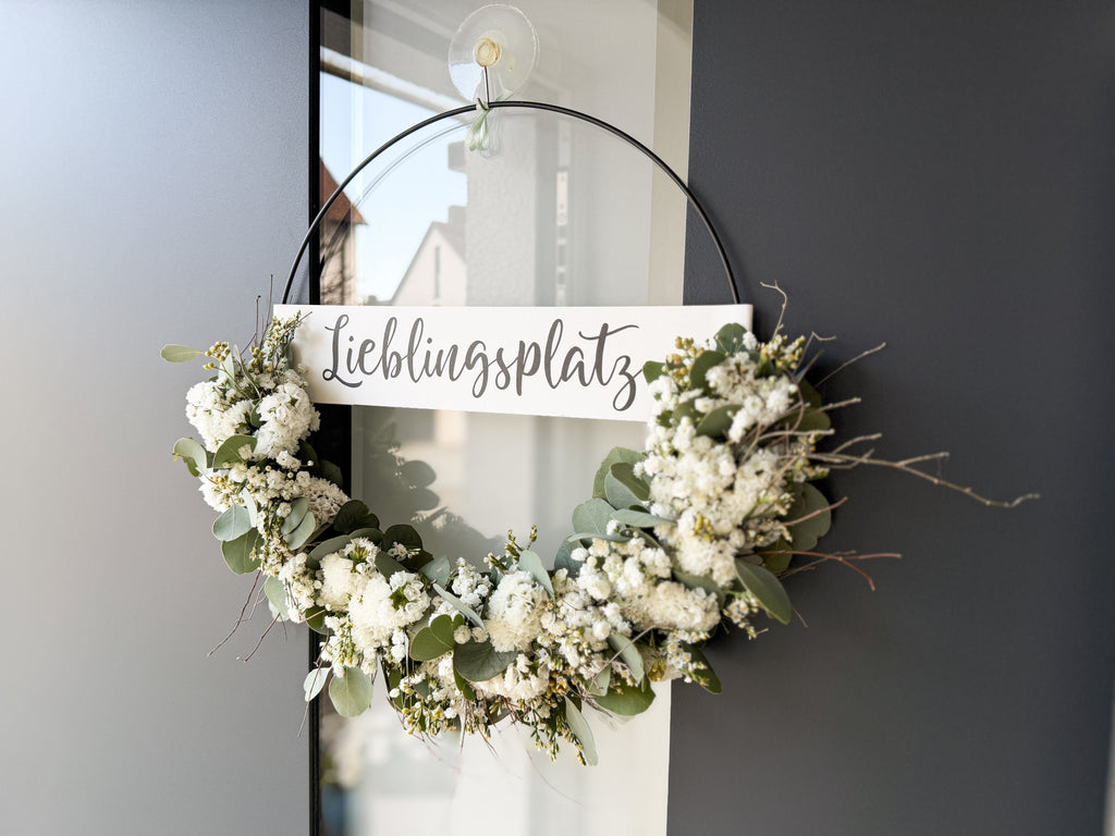 Moderner FlowerLoop mit weißen Blüten und Eukalyptus an dunkler Haustüre – Türkranz mit Schriftzug „Lieblingsplatz“ - Querformat