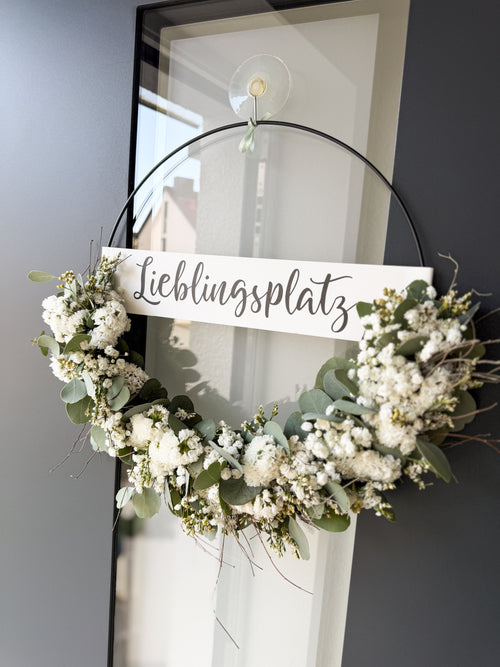 Moderner FlowerLoop mit weißen Blüten und Eukalyptus an dunkler Haustüre – Türkranz mit Schriftzug „Lieblingsplatz“.