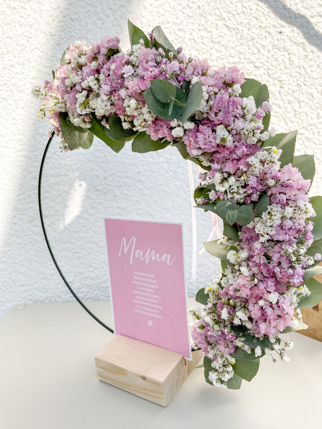 1/2 Flowerloop mit Eukalyptus, Blüten und Postkarte „Mama“ auf Holzständer als Muttertagsdeko