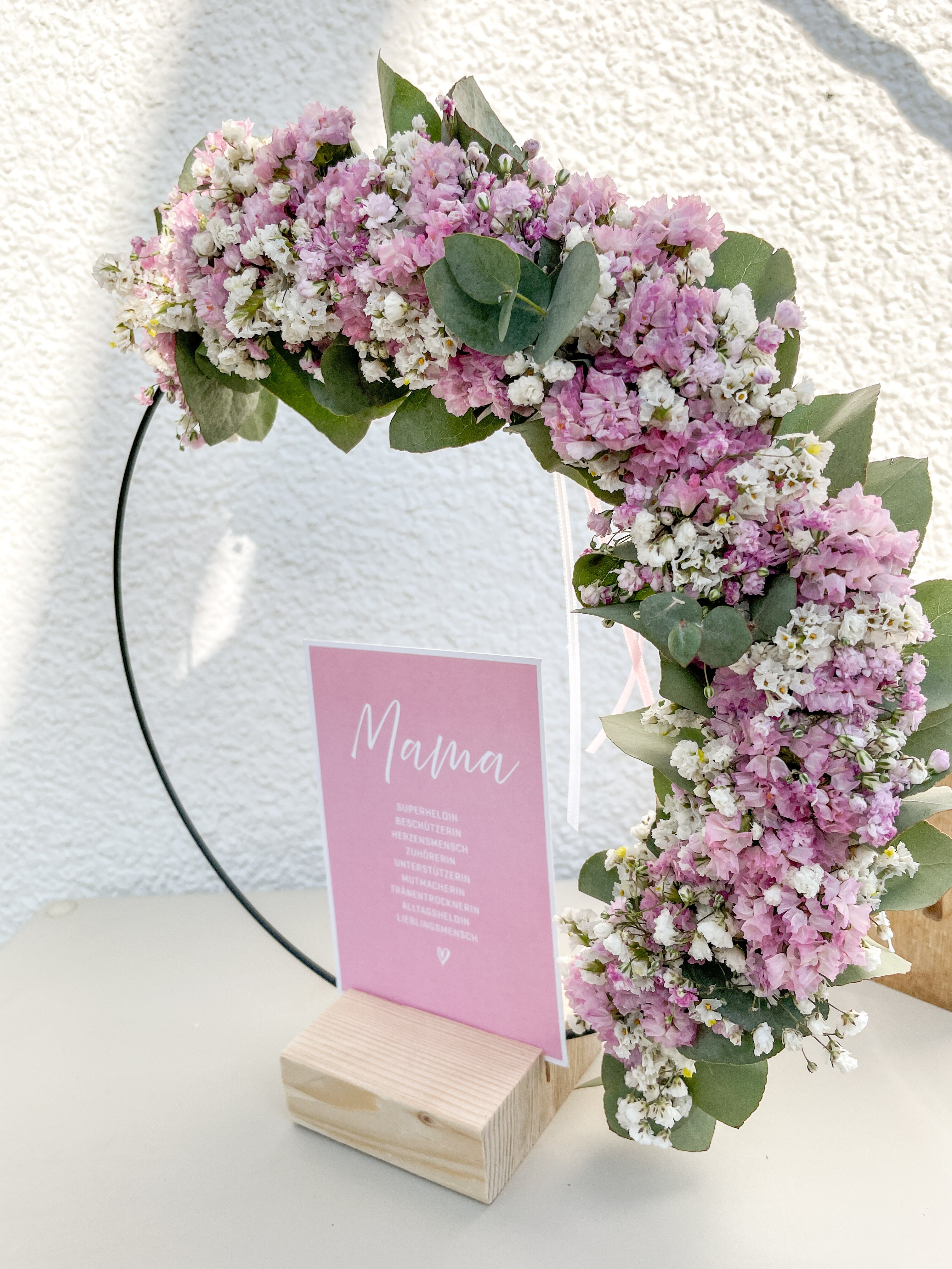 1/2 Flowerloop mit Eukalyptus, Blüten und Postkarte „Mama“ auf Holzständer als Muttertagsdeko