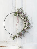 1/2 Loop »Vertical Soft Spring« – vertikal gebundener Metallring mit Eukalyptus, weißen und rosa Blüten, Satinbändern in Weiß und Rosa sowie hängendem Metallherz