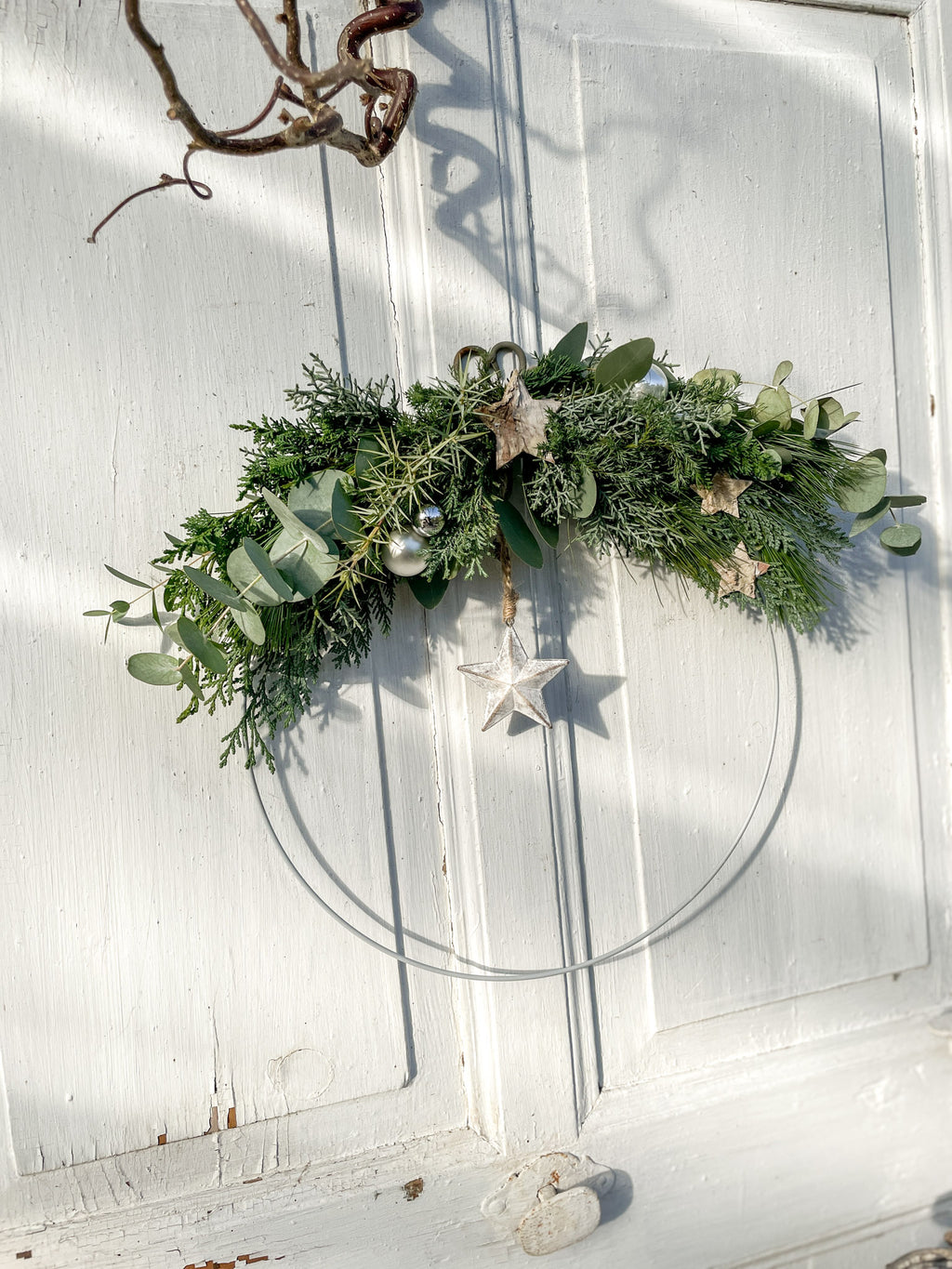 1/2 Winter-Loop ‚Evergreen Canopy‘ Hochformat, Metallring halbseitig dekoriert mit Eukalyptus- und Koniferengrün, Zweige überragen oberen Rand, Lerchenzapfen, Birkensterne, Dekokugeln