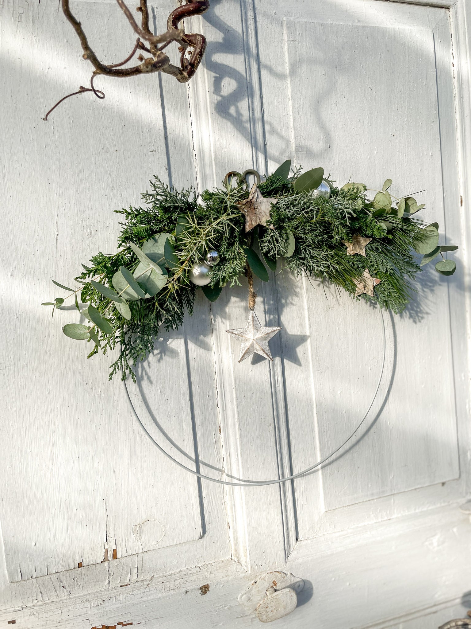 1/2 Winter-Loop ‚Evergreen Canopy‘ Hochformat, Metallring halbseitig dekoriert mit Eukalyptus- und Koniferengrün, Zweige überragen oberen Rand, Lerchenzapfen, Birkensterne, Dekokugeln