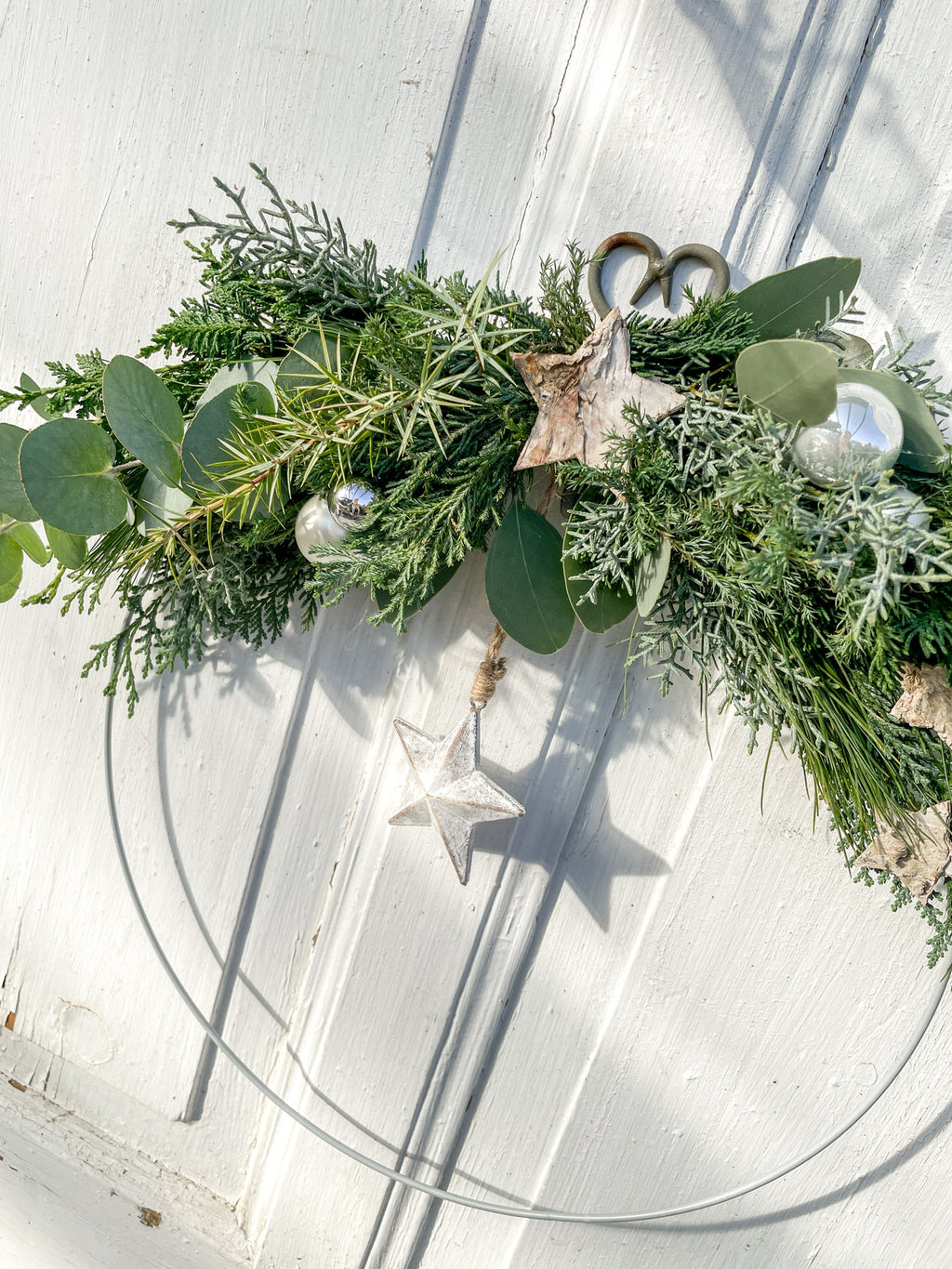 1/2 Winter-Loop ‚Evergreen Canopy‘ Hochformat von Oben, Metallring halbseitig dekoriert mit Eukalyptus- und Koniferengrün, Zweige überragen oberen Rand, Lerchenzapfen, Birkensterne, Dekokugeln