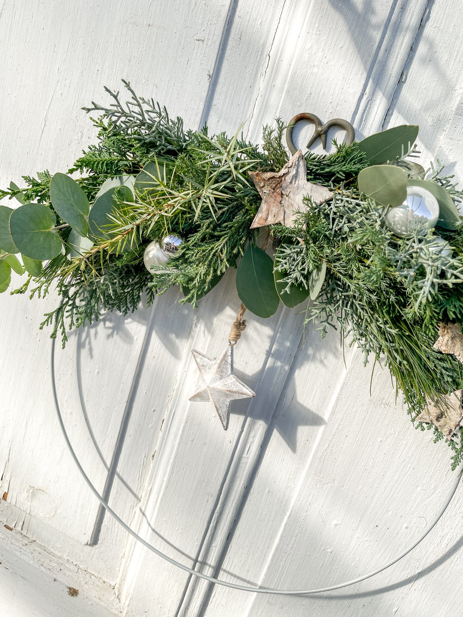 1/2 Winter-Loop ‚Evergreen Canopy‘ Hochformat von Oben, Metallring halbseitig dekoriert mit Eukalyptus- und Koniferengrün, Zweige überragen oberen Rand, Lerchenzapfen, Birkensterne, Dekokugeln