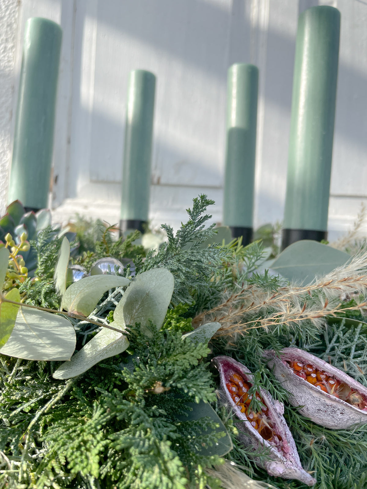 Detailansicht Material von Adventskranz »Emerald« im warmen Licht mit smaragdgrünen Stabkerzen, getrockneten Maracujas und Dekokugeln