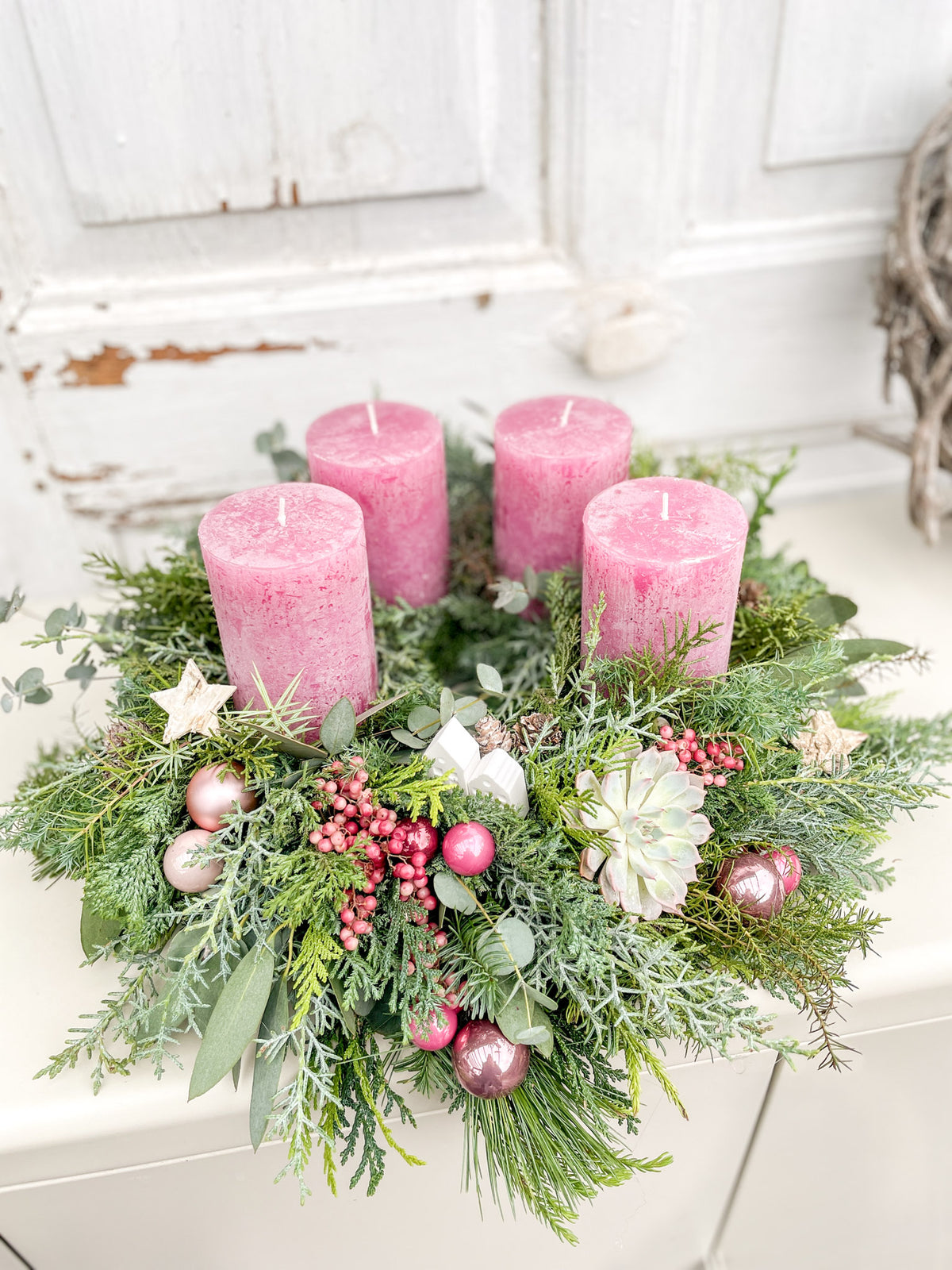 Stimmungsbild Adventskranz »Rosenrot« mit rosaroten Kerzen und weißen Häuschen im warmen Licht