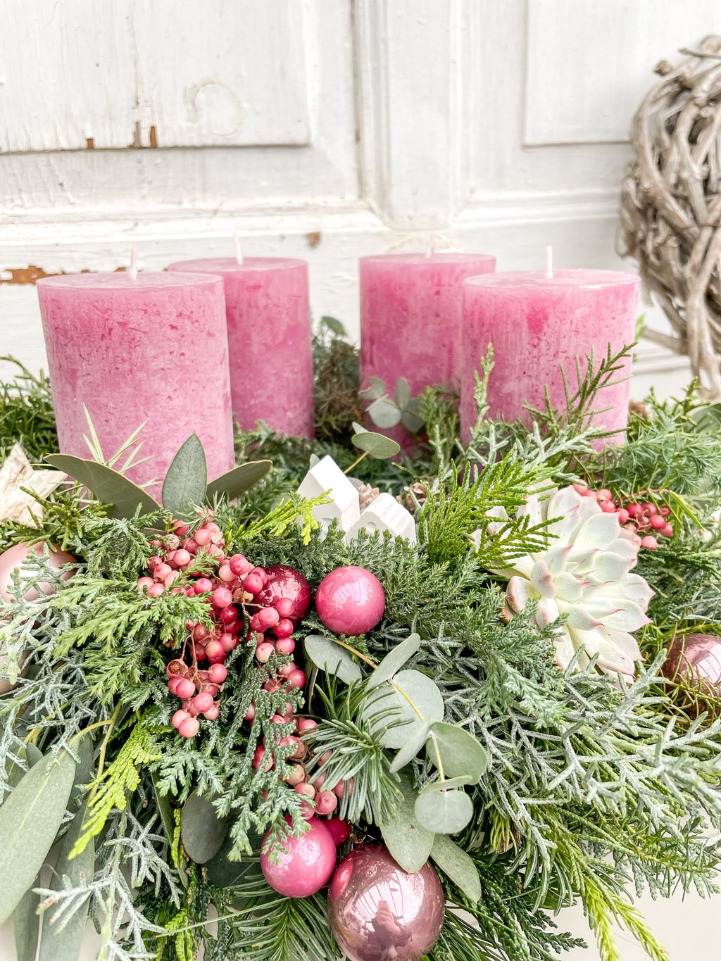 Nahaufnahme: rosarote Stumpenkerze, Dekokugeln in Beerentönen, rote Pfefferbeeren und kleine Zapfen am Adventskranz
