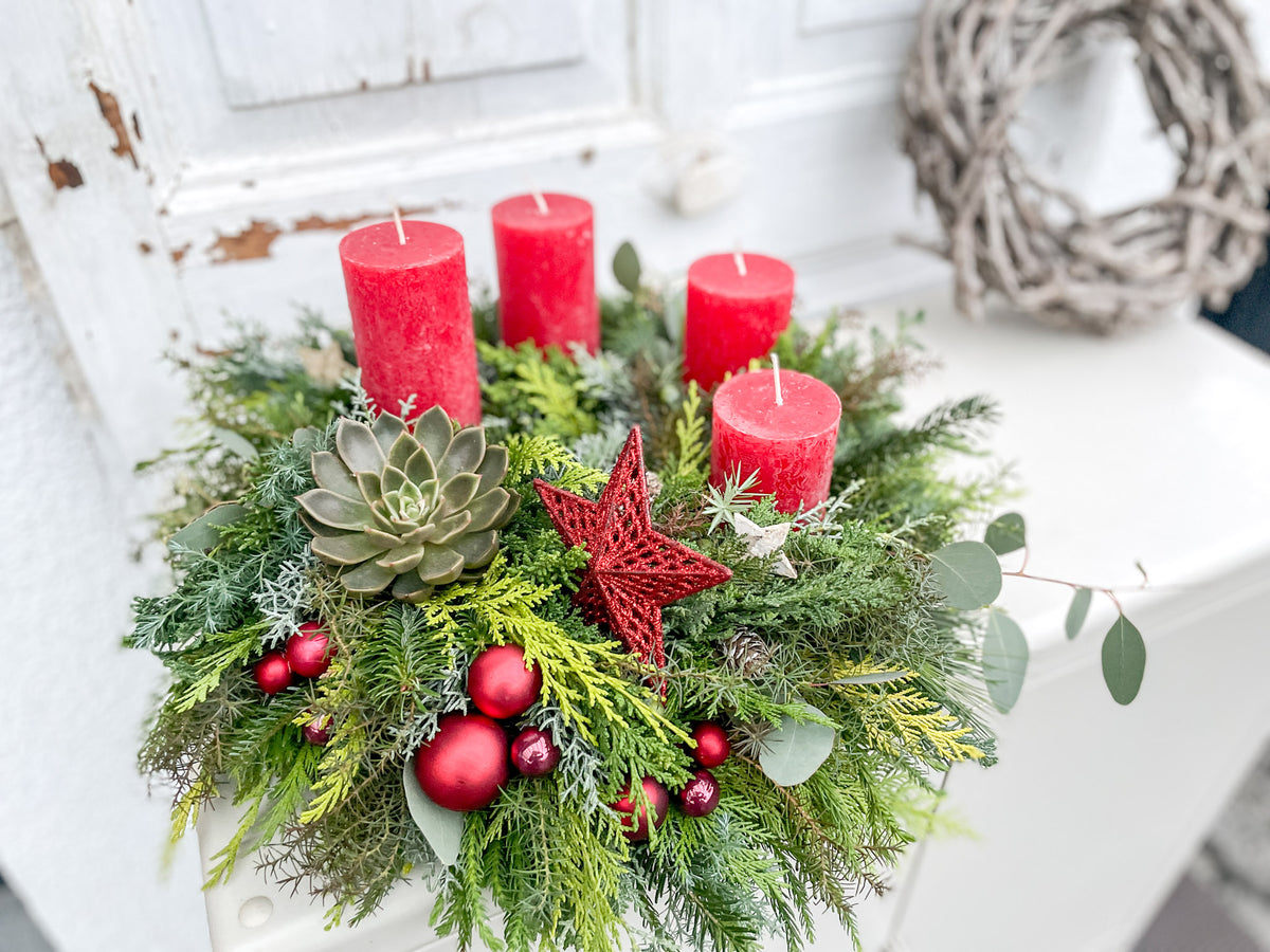 Vier rote Stumpenkerzen in aufsteigender Höhe am Adventskranz »Winterrot«, umgeben von Nadelgrün und Zapfen