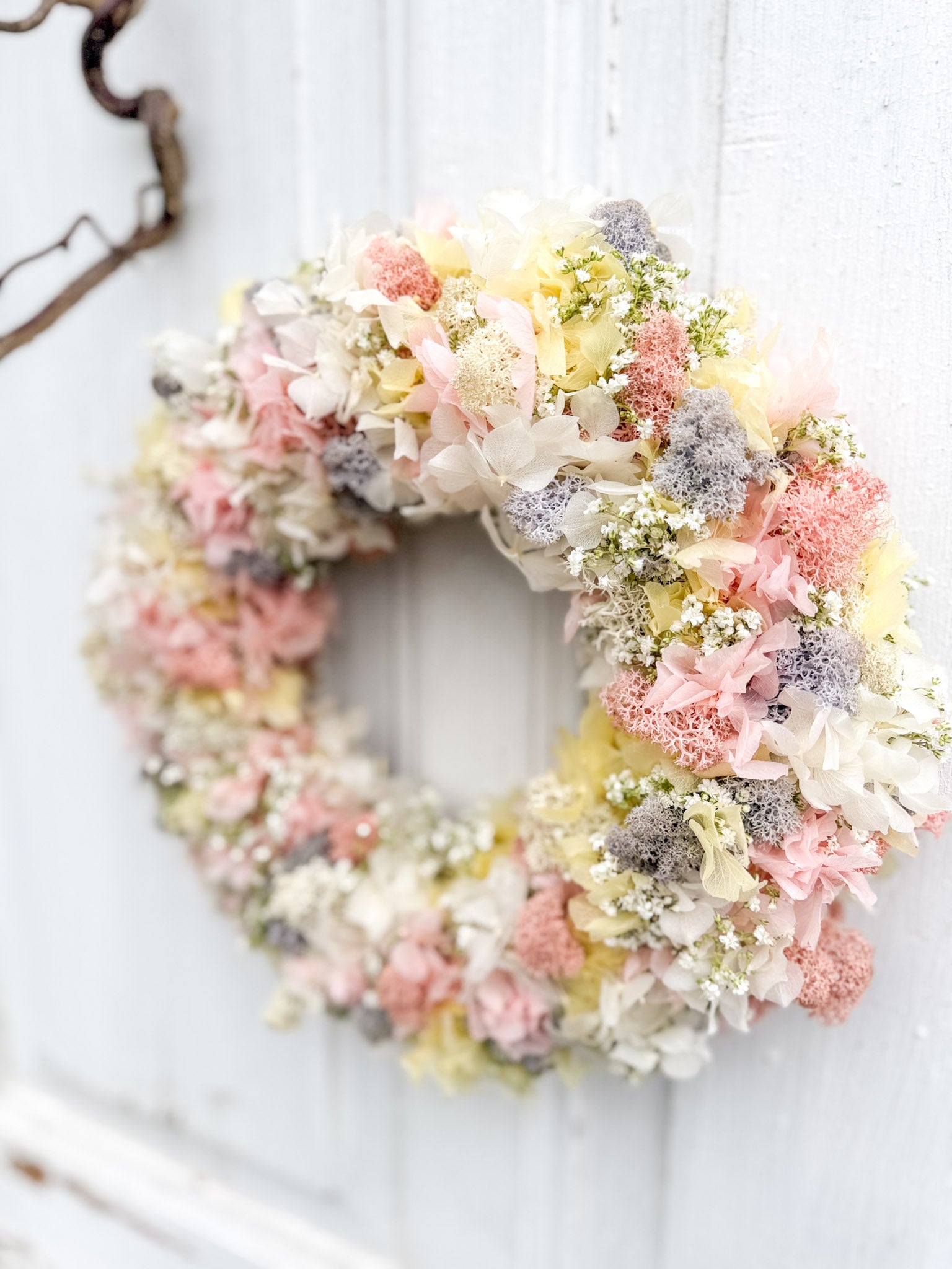 Frühlings-Blumenkranz »Pastell Bloom« auf Tisch arrangiert, pastellfarbene Hortensien, Islandmoos, weiße Schleierkraut-Akzente, stilvolle Frühlingsdeko