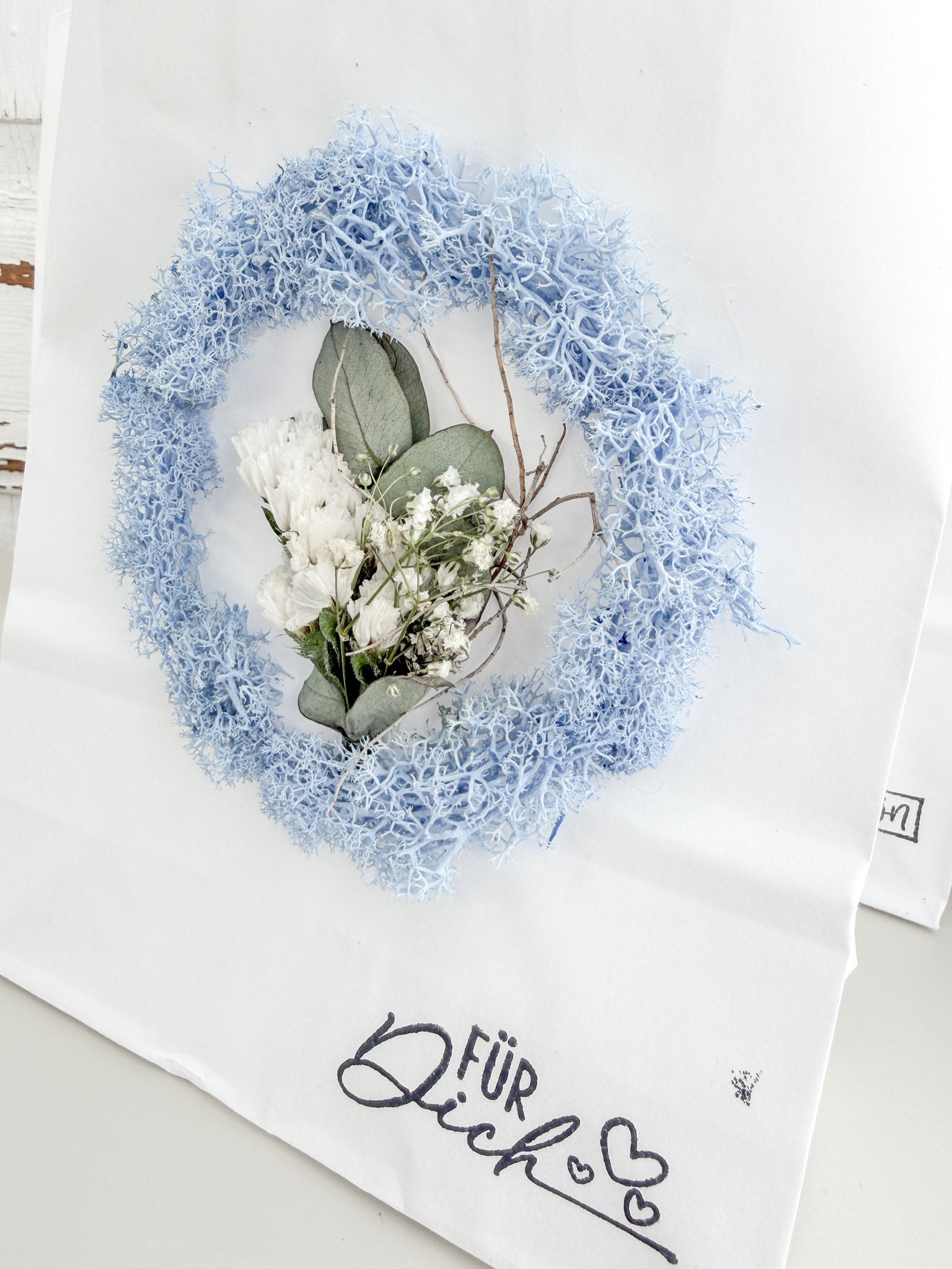 Detailaufnahme Mini-Mooskranz aus konserviertem Islandmoos mit mittig arrangiertem Mini-Bouquet auf Geschenktüte