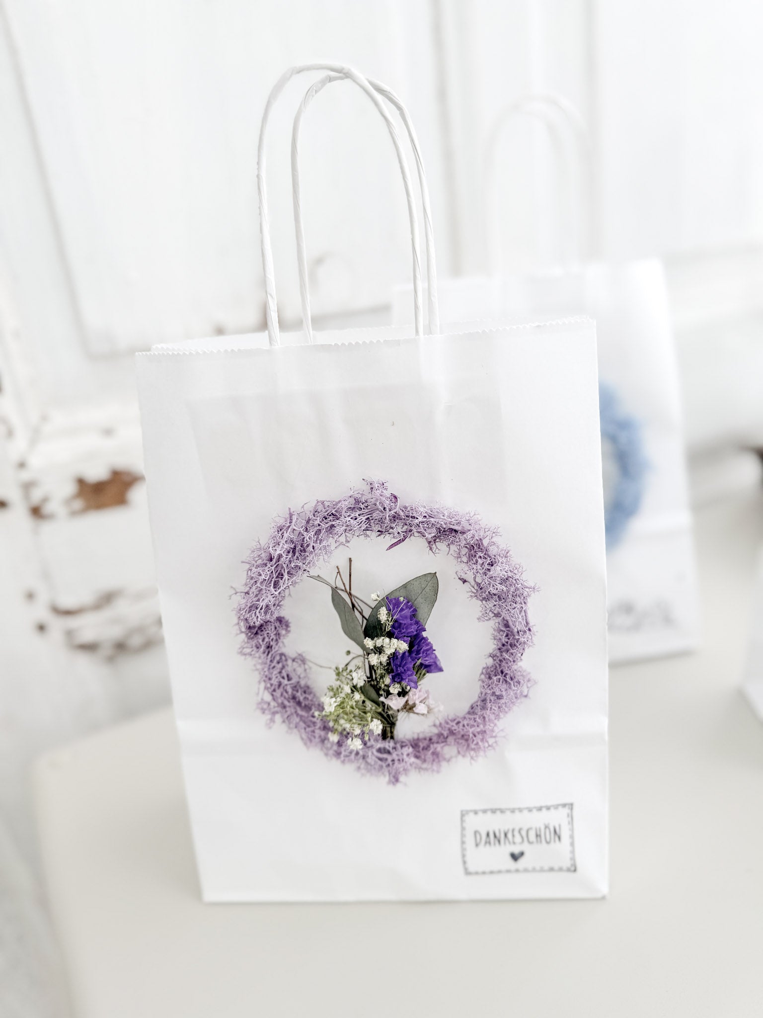 Detailaufnahme Mini-Mooskranz aus konserviertem Islandmoos mit mittig arrangiertem Mini-Bouquet auf Geschenktüte