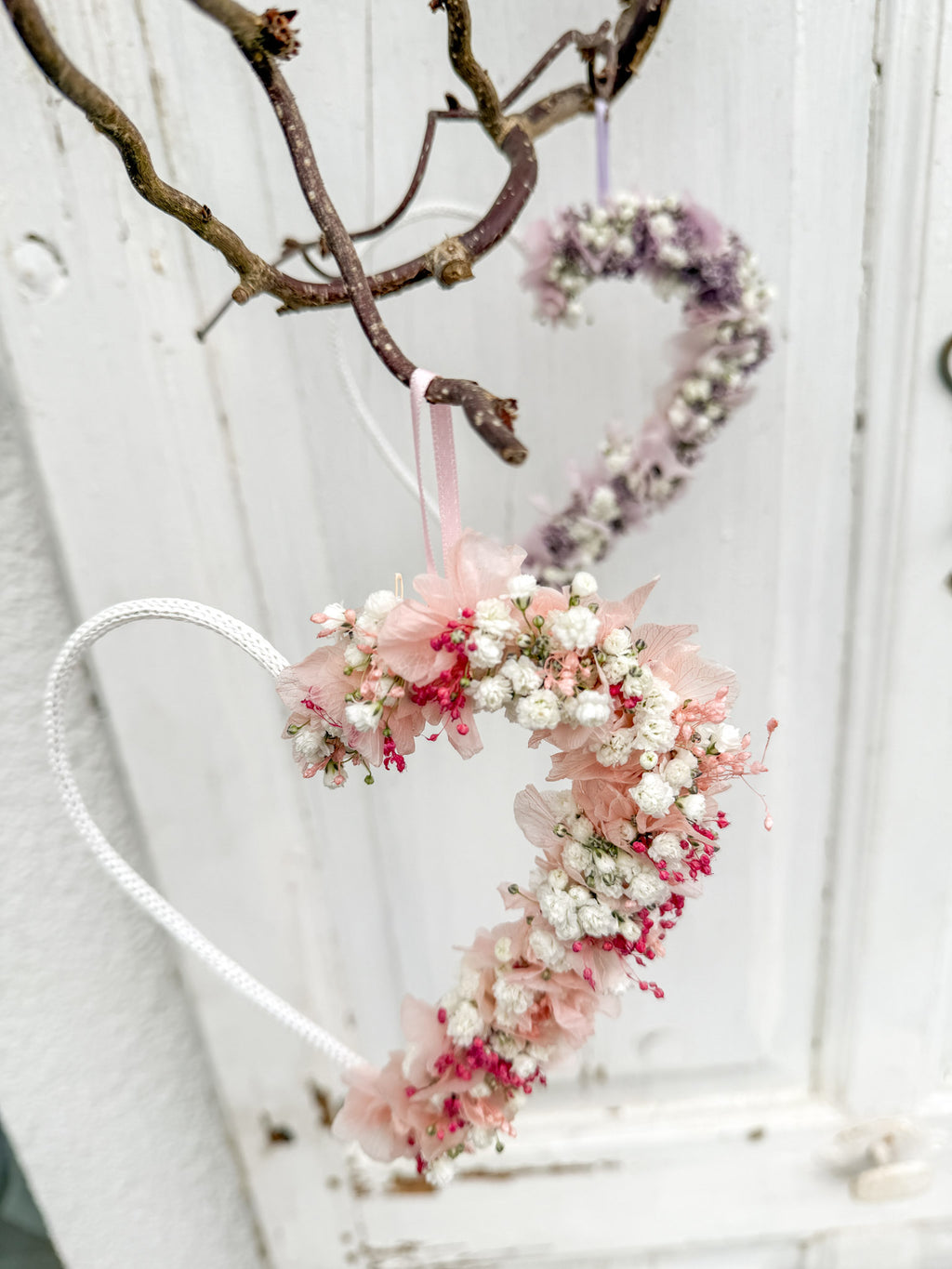 Detail im Hochformat: Herz hängt an Wand, halb mit Blüten dekoriert
