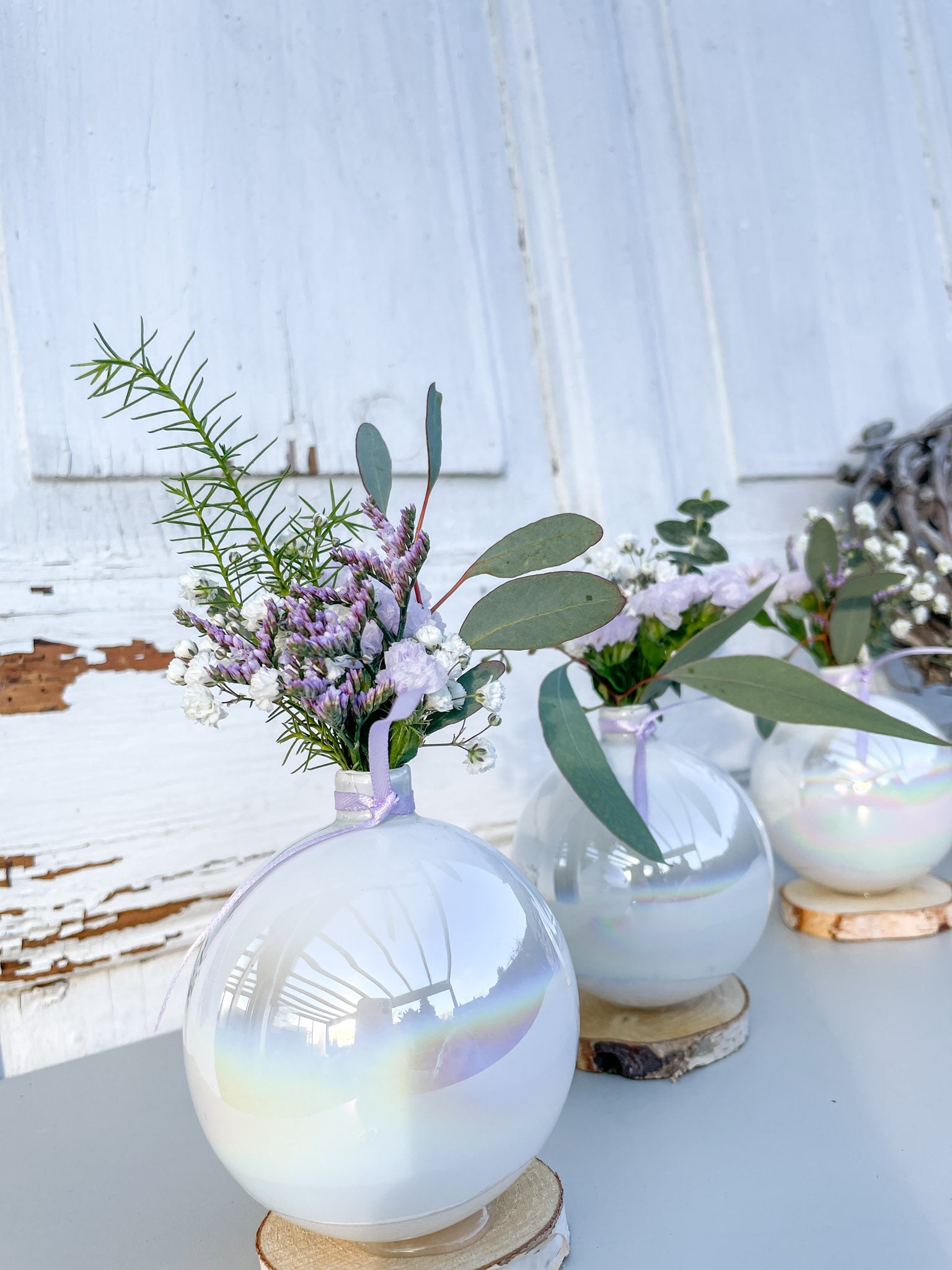 Christbaumkugel-Vase ‚Lila Blütenzauber‘ Hochformat, Glasvase mit Perlmutschimmer auf Holzscheibe, gefüllt mit Mini-Bouquet aus lila Blüten und Eukalyptus