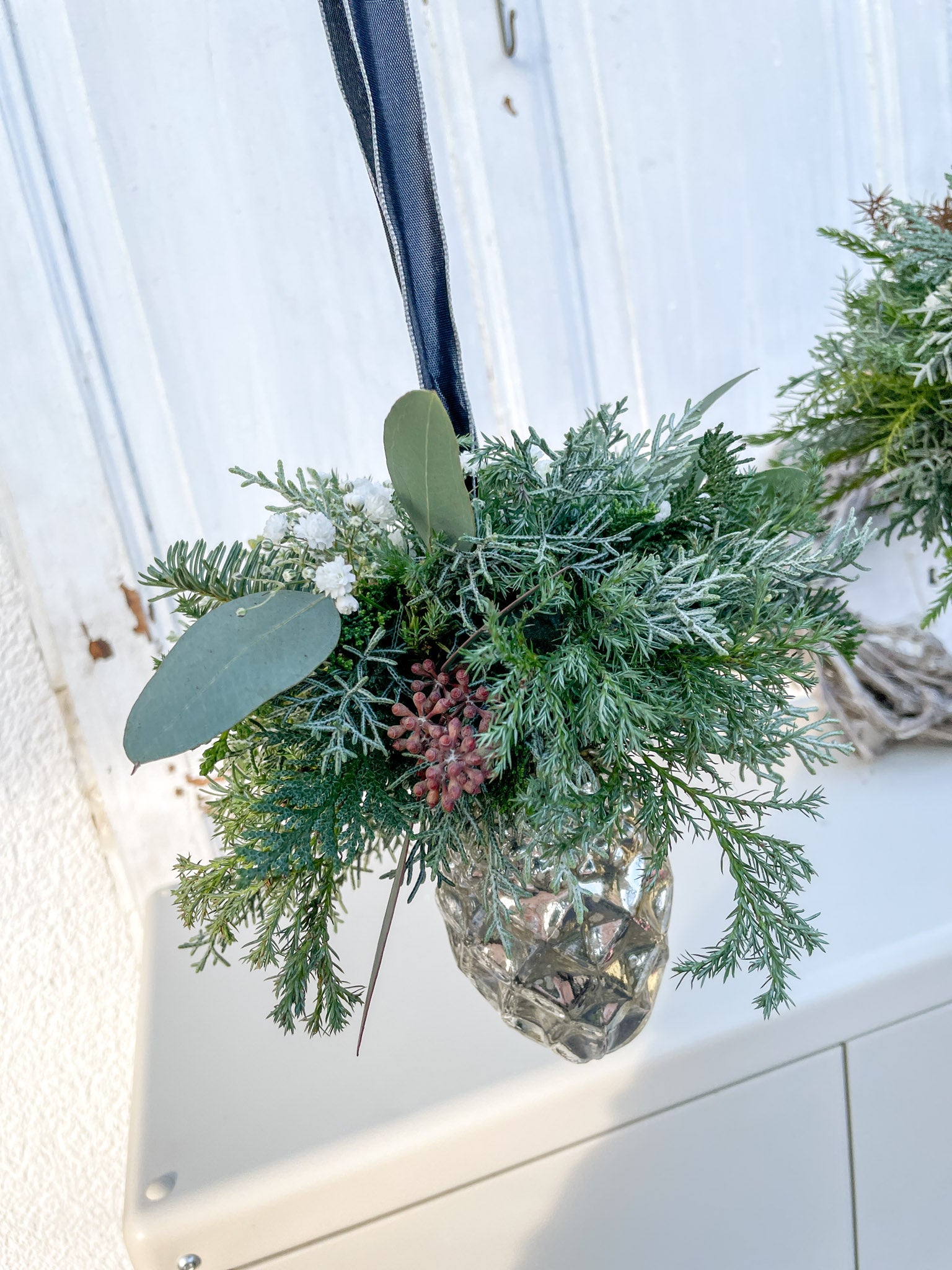Detailaufnahme des Mini-Bouquets aus Nadel- und Koniferengrün, Eukalyptus und weißem Schleierkraut auf Glaszapfen ‚Winter Elegance