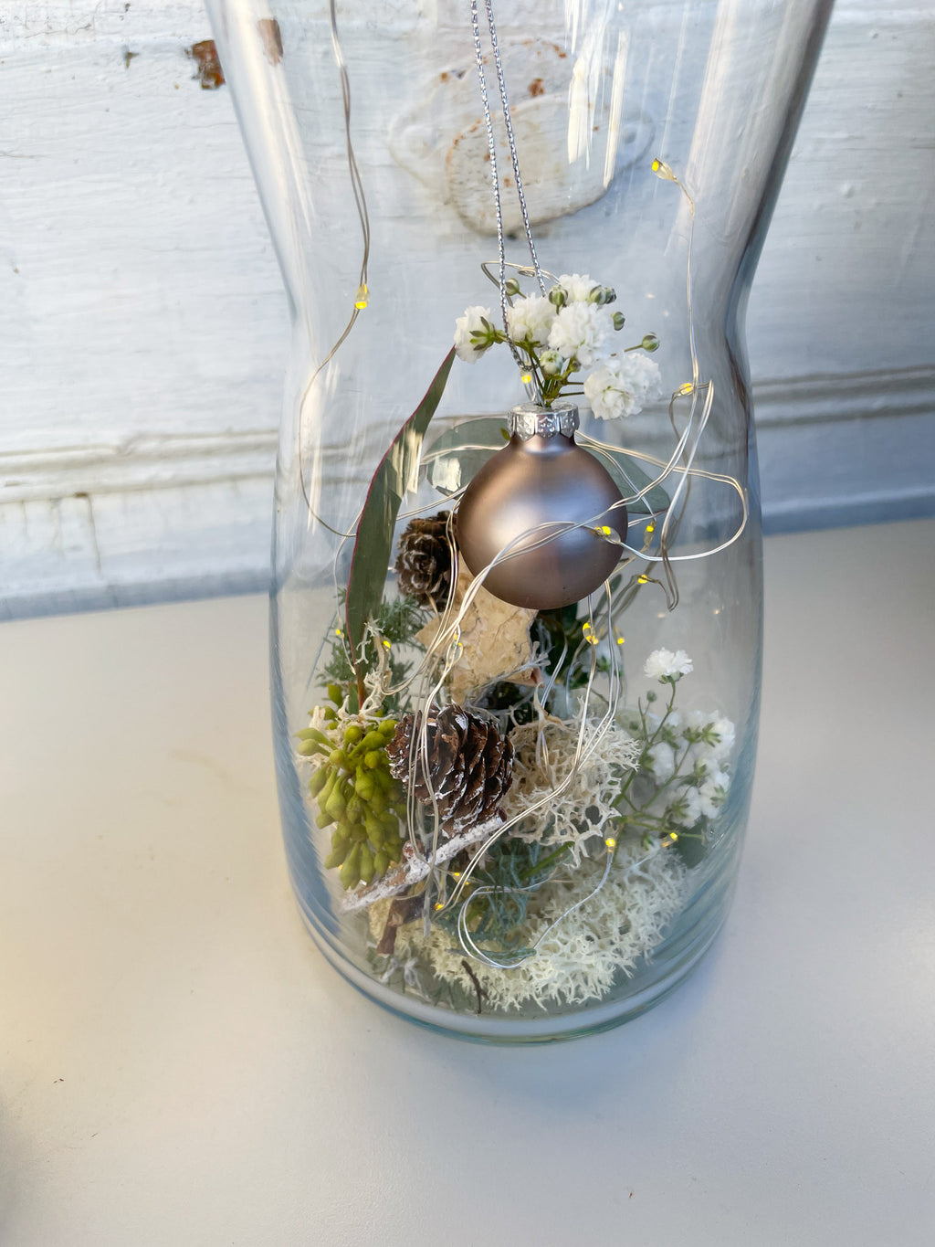 Nahaufnahme Glasvase Winterzauber, Nadelgrün, Eukalyptus, Zapfen, Islandmoss, goldener Deckel mit Anthrazit-Kugel