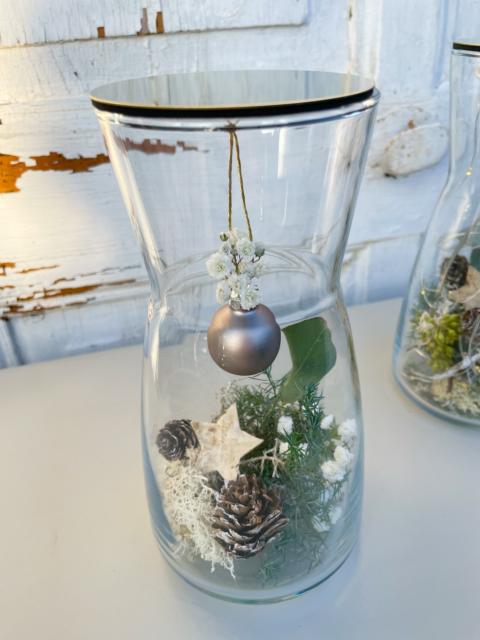 Nahaufnahme Glasvase Winterzauber, Nadelgrün, Eukalyptus, Zapfen, Islandmoss, goldener Deckel mit Anthrazit-Kugel, winterliche Tischdekoration