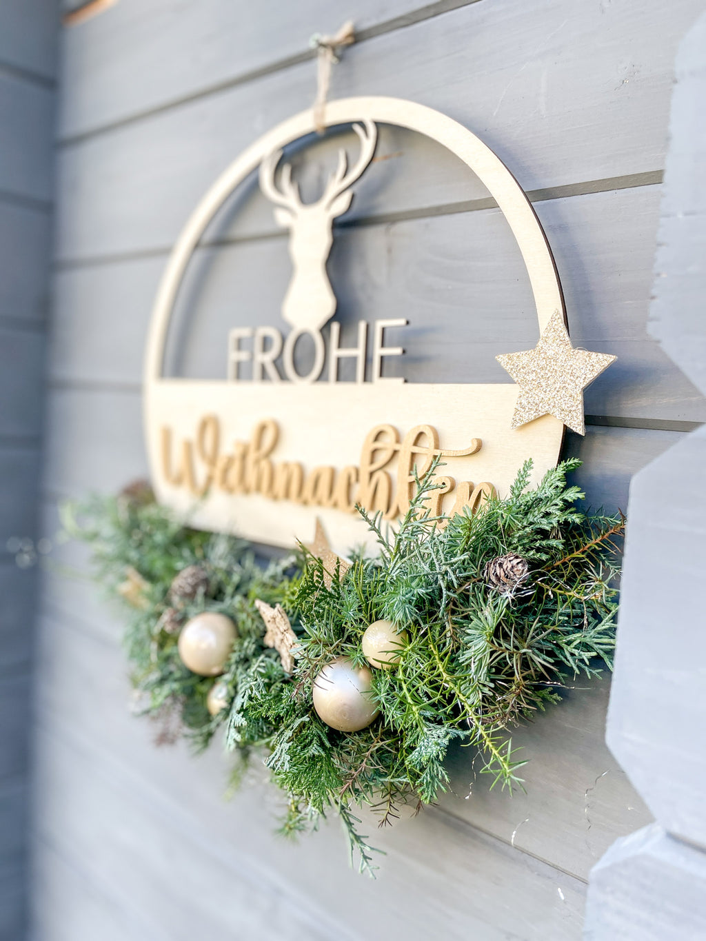 Detailaufnahme von Material und Kugeln in Gold- und Cremetönen, Birkensternen und Lerchenzapfen auf dem Holzloop ‚Frohe Weihnachten‘