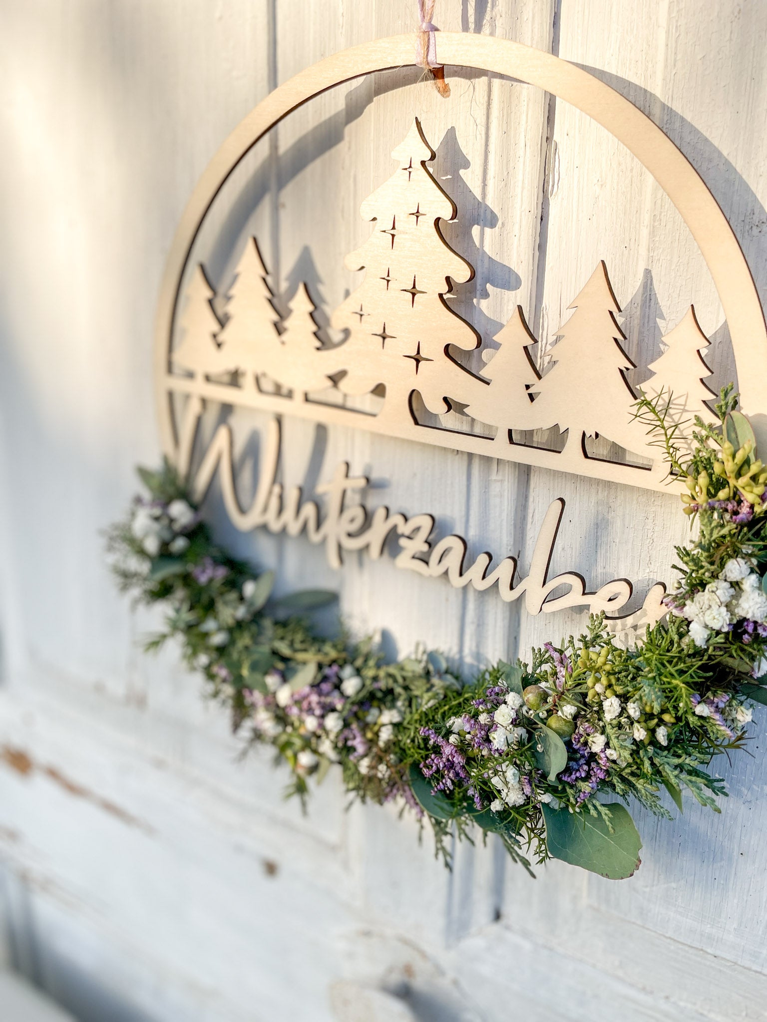Winterlicher Holzloop Winterzauber mit Holzschriftzug, Koniferengrün, Eukalyptus und lila Strandflieder, Ø 25–30 cm, vor weißer Wand