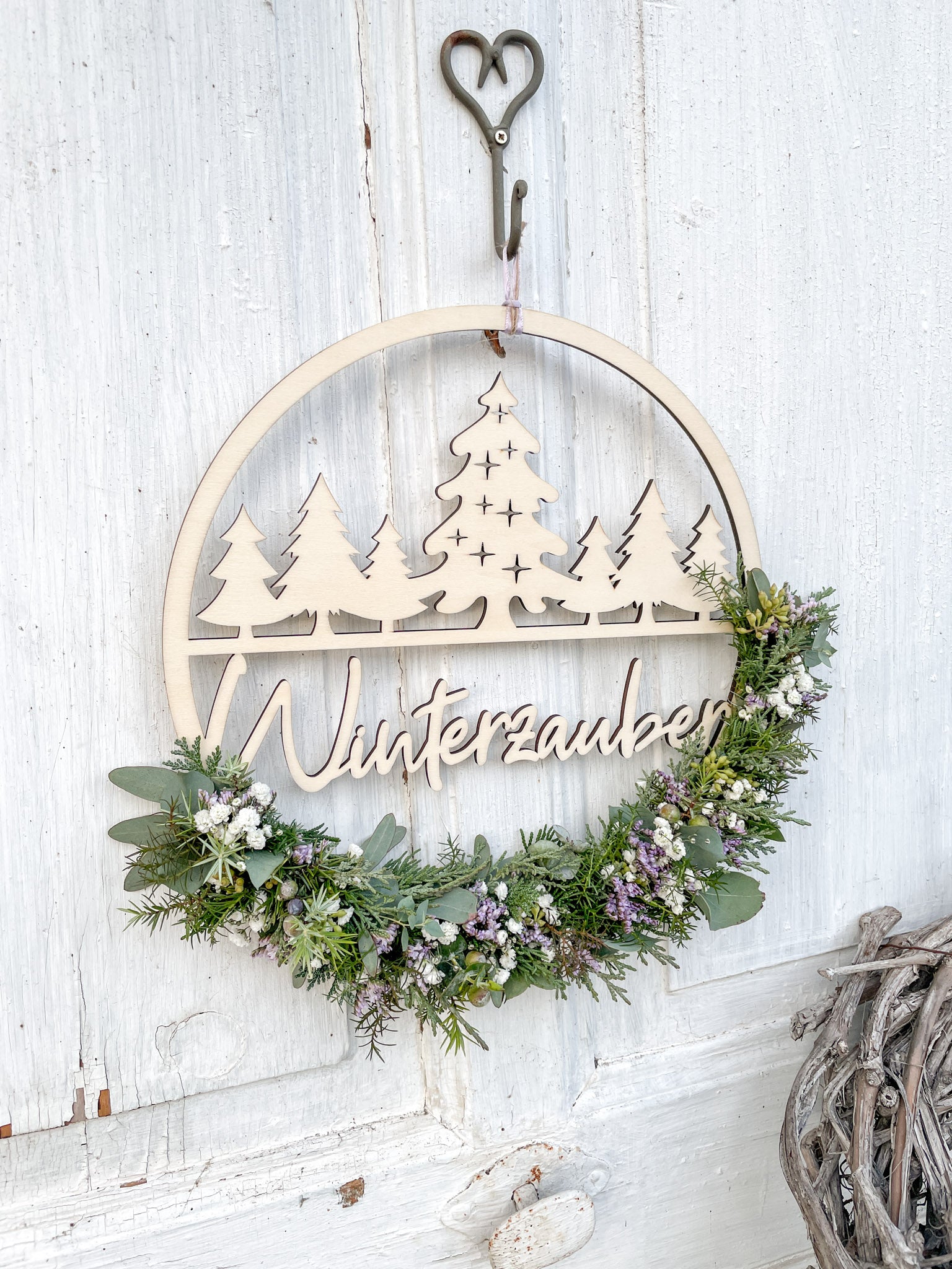 Winterlicher Holzloop Winterzauber mit Holzschriftzug, Koniferengrün, Eukalyptus und lila Strandflieder, Ø 25–30 cm, vor weißer Wand