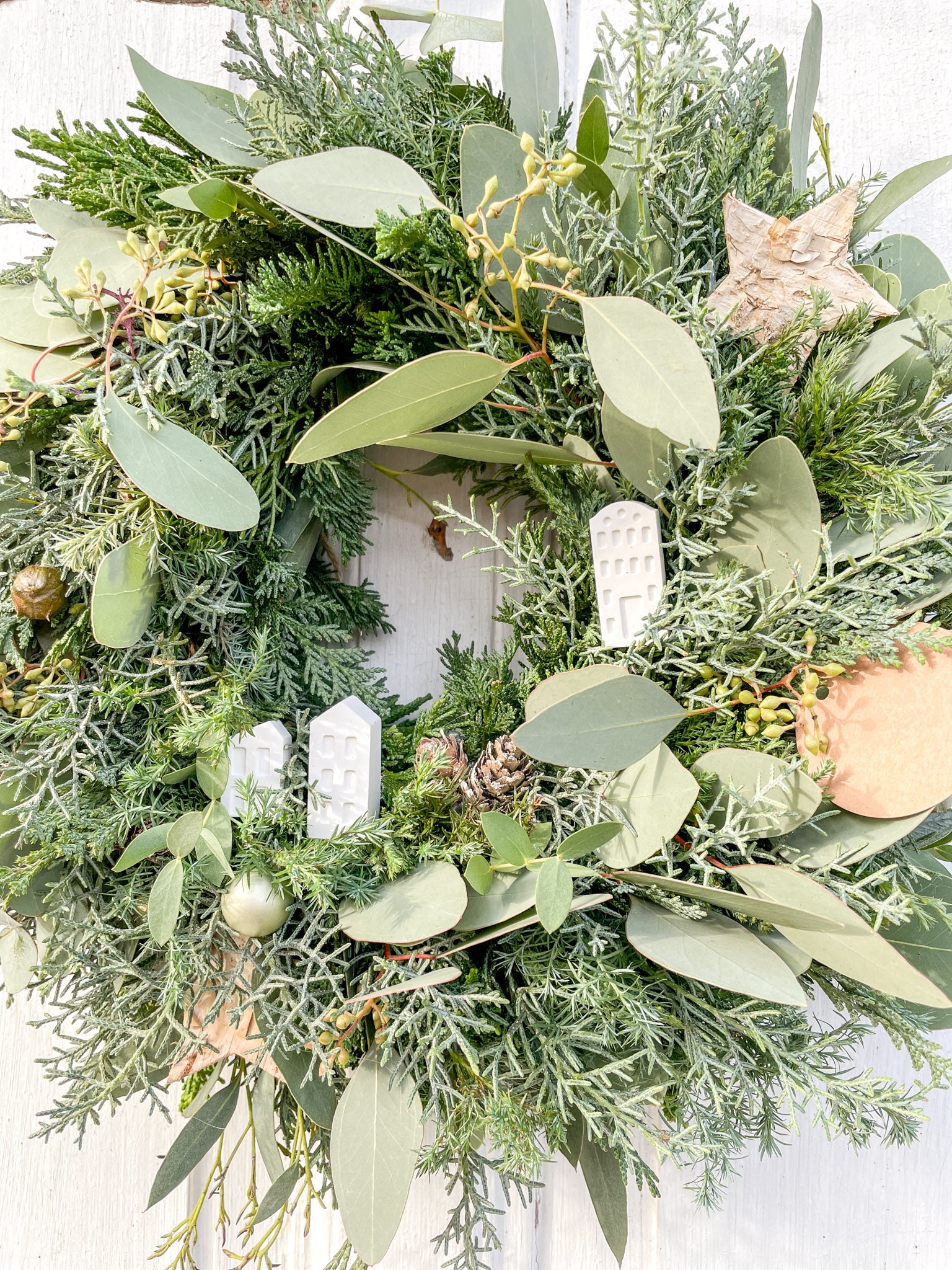 Nahaufnahme der Tannen-, Koniferengrün- und Eukalyptus-Zweige des Winterkranzes ‚Frosty Village‘, stabilisierte Materialien für langanhaltende winterliche Dekoration