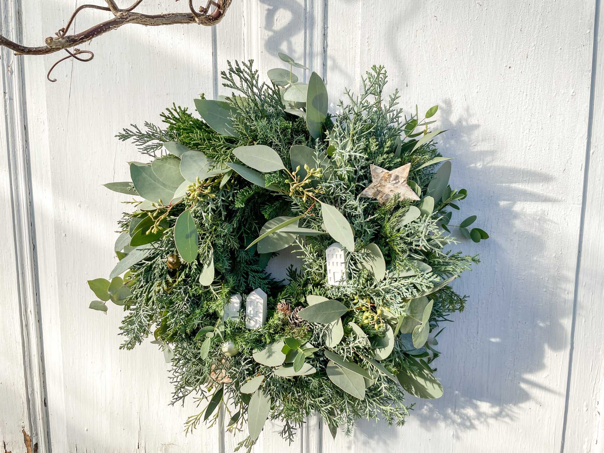 Winterkranz ‚Frosty Village‘ in Querformat, minimalistisches Design mit grünem Tannen- und Koniferengrün, Eukalyptus und weißen Resin-Häusern, ideal für Tisch- oder Wanddekoration